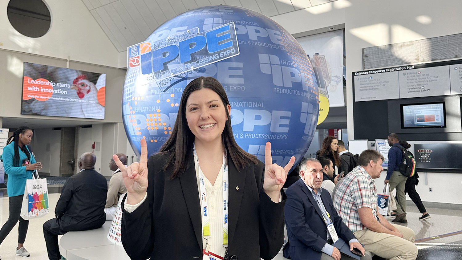a woman making wolfy signs with her hands stands in front of a globe with the logo IPPE on it