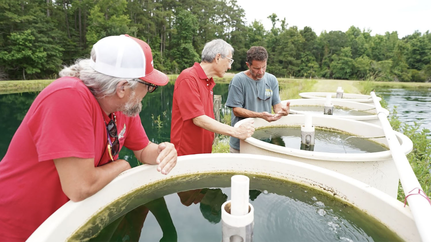 three men look at holding tanks next to a pond